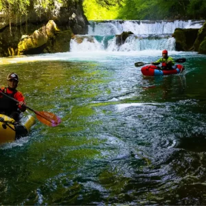 osobe u packraft čamcu veslaju na rijeci Mrežnici sa slapovima u pozadini