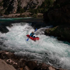 A person in a red packraft, paddling and going down a rapid on Zrmanja river
