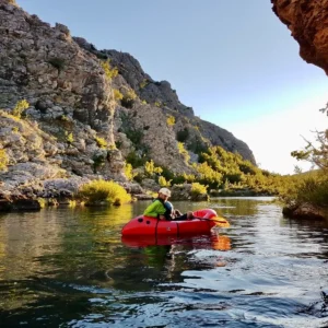 A person, sitting in a red packraft while adjusting his straps