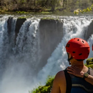 Picture of 2 people hugging with the tall waterfall in the background on Zrmanja river