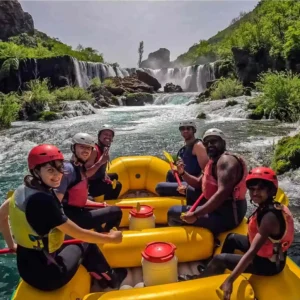 Grupa ljudi u raft čamcu sa visokim slapom u pozadini