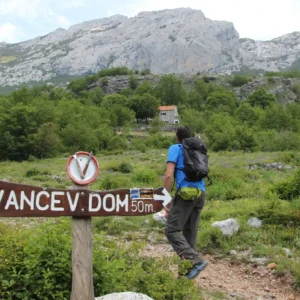 Group of people hiking on Paklenica and a big sign for a mountain hut in the foreground