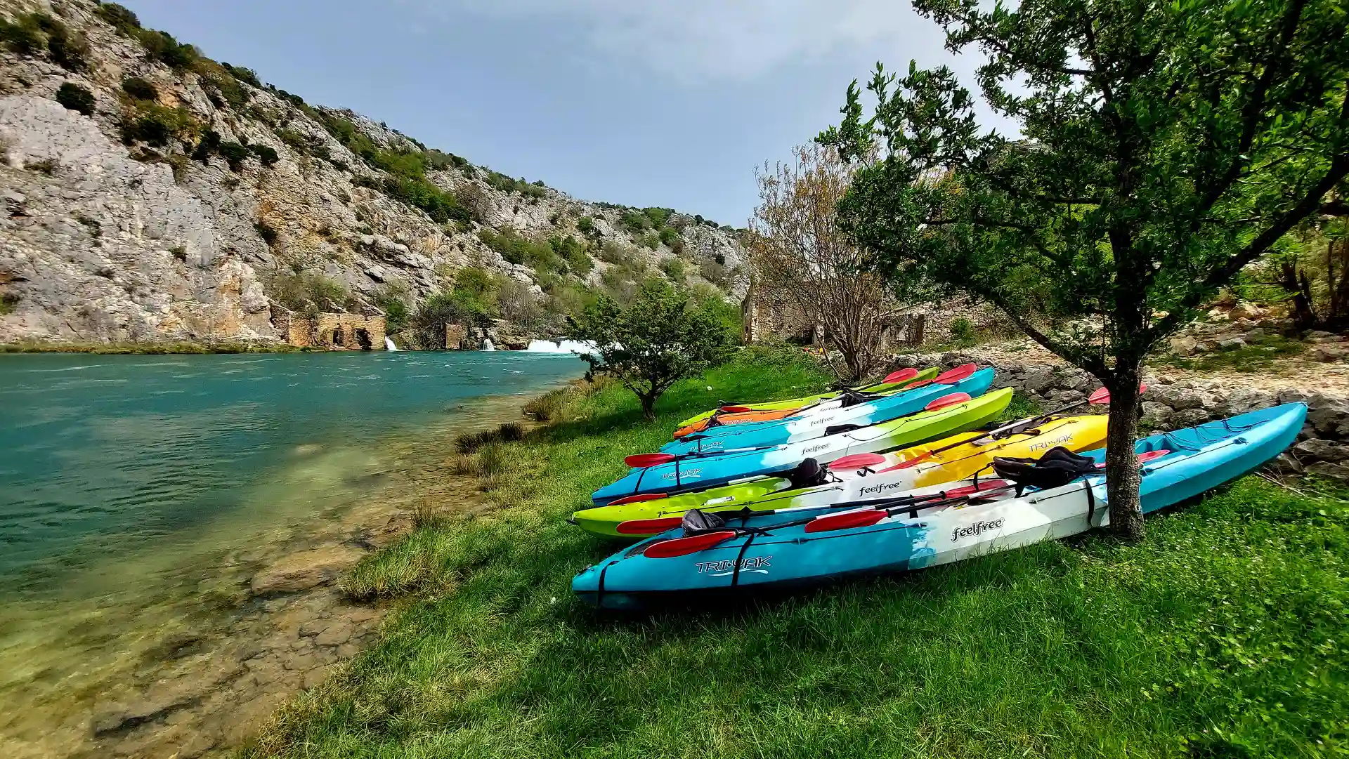 Sea kayaks on the side of the river with the waterfall in the background