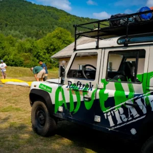 Land Rover Defeneder sa npisom "raftrek" i vodiči u pozadini koji pripremaju opremu